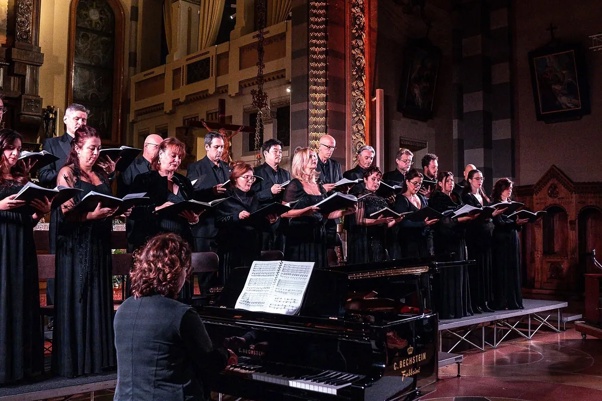 Il coro canta con lo spartito in mano accanto al pianoforte Bechstein, nella chiesa del Sacro Cuore illuminata di rosso e oro