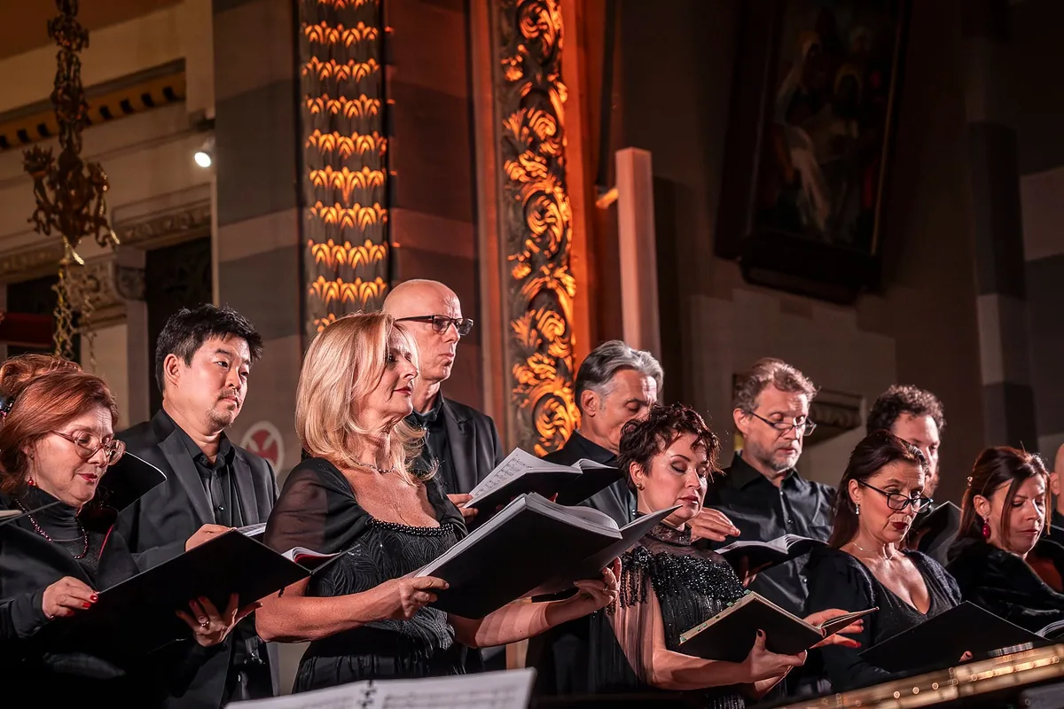 Coriste e coristi del Coro Pergolesi cantano con lo spartito in mano, in una chiesa dalle colonne dorate